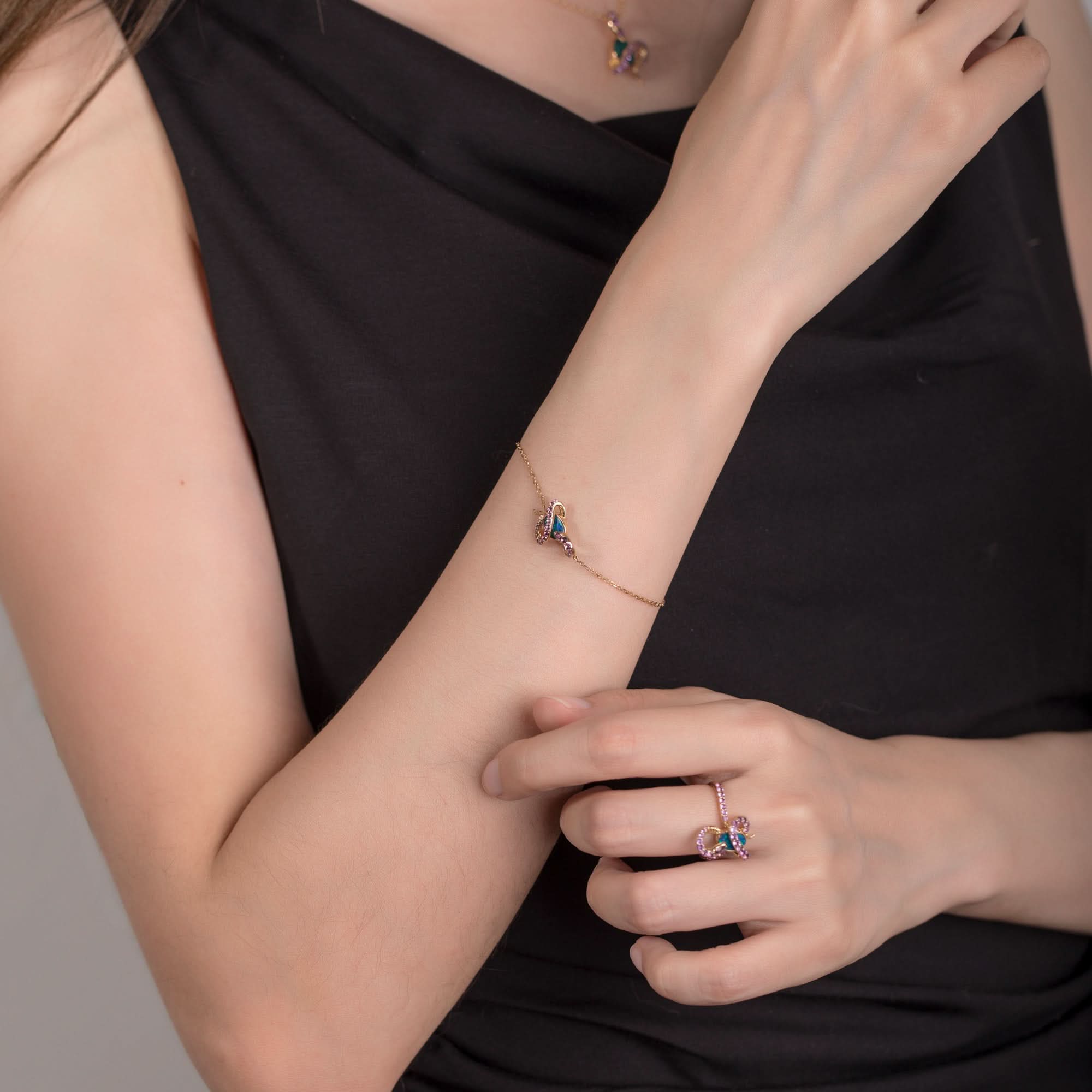 A model wearing an 18K gold Australian opal bracelet featuring a delicate gold chain and a snake design adorned with amethyst gemstones. The matching opal ring and pendant necklace complete the elegant and cohesive jewelry set. The opal’s vibrant blue-green hues contrast beautifully with the rich purple of the amethysts, creating a luxurious and sophisticated look.