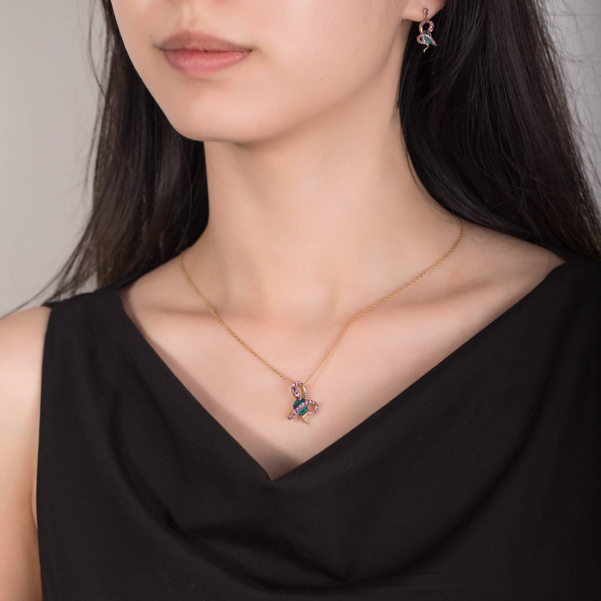 A model wearing an 18K gold Australian opal pendant necklace featuring a snake design adorned with natural amethyst gemstones. The opal’s vibrant blue-green hues contrast beautifully with the rich purple amethysts and yellow gold setting. The model also wears matching snake-design opal earrings, creating a cohesive and elegant jewelry set.