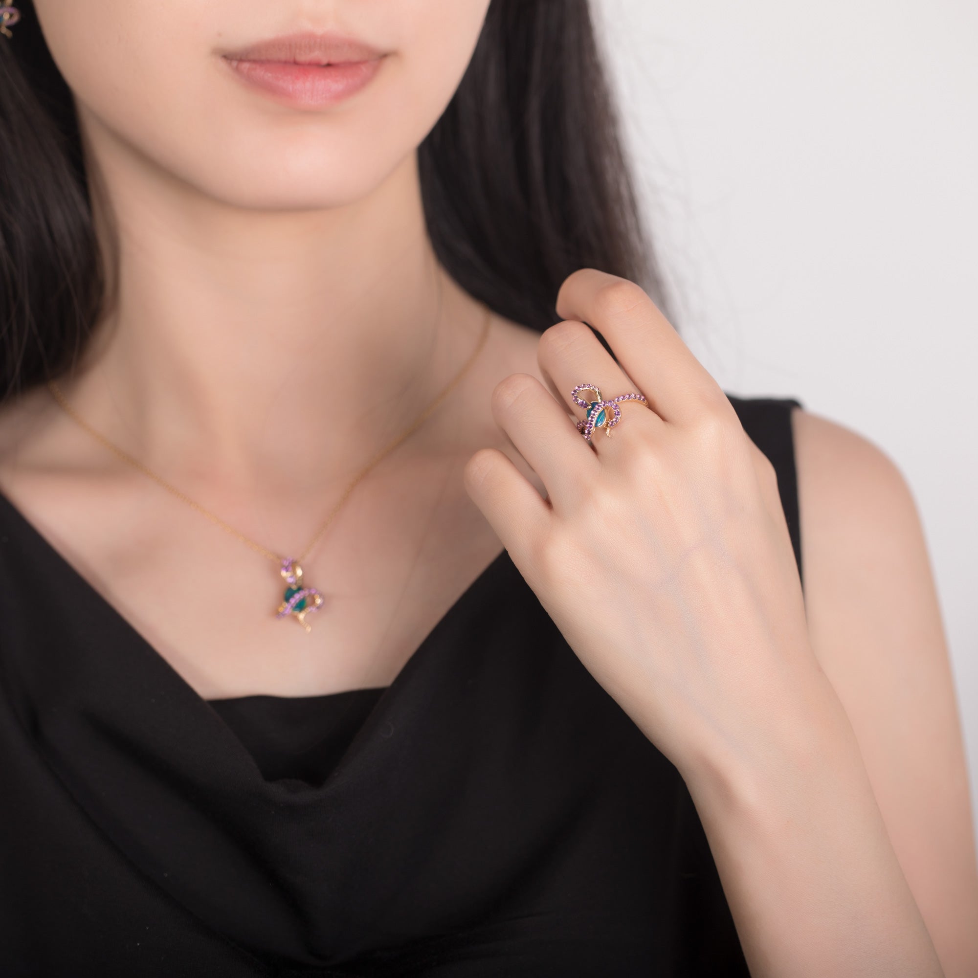 A model wearing an 18K gold Australian opal ring with a snake design, featuring a vibrant oval opal and amethyst gemstones. The matching opal pendant necklace complements the ring, creating a sophisticated and elegant look. The jewelry is set in yellow gold, enhancing the rich colors of the gemstones.